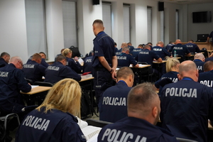 policjanci rozwiązują pisemnie kazus siedząc na krzesłach przy ławkach