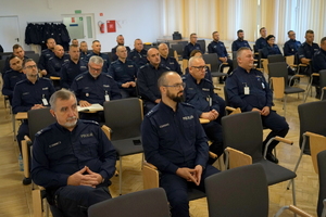 policjanci siedzą na krzesłach, słuchają organizatorów zawodów i przystępują do pisania testu