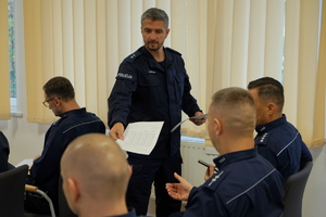 policjanci siedzą na krzesłach, słuchają organizatorów zawodów i przystępują do pisania testu