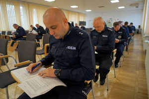 policjanci siedzą na krzesłach, słuchają organizatorów zawodów i przystępują do pisania testu