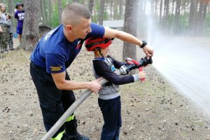 Strażak pokazuję różne możliwości puszczania wody z  węża strażackiego.