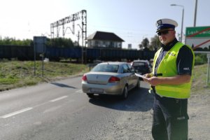 Policjant obserwuje ruch drogowy w rejonie przejazdu kolejowego