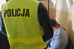 Policjant pilnuje zatrzymanego do odbycia kary poszukiwanego