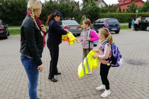 Policjantka przekazuje kamizelki dzieciom