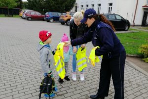 Funkcjonariuszka wręcza dzieciom kamizelki odblaskowe