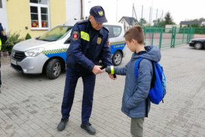 Strażnik miejski zakłada uczniowi opaskę odblaskową