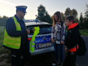 Policjant wręcza kamizelki odblaskowe dzieciom