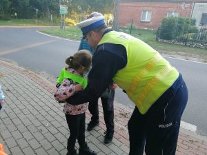 Policjant pomaga założyć dziewczynce odblaski