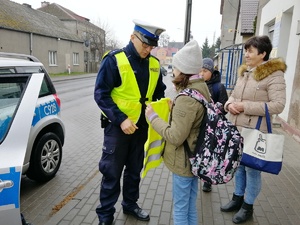 Policjant wręcza kamizelkę pieszej dziewczynce