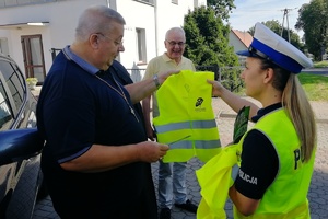 Poza pojazdem stoi kierowca, policjantka wręcz mi kamizelkę odblaskową