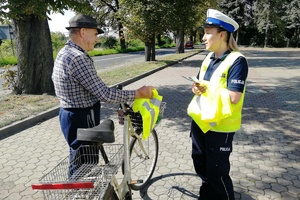 Mundurowa rozmawia z rowerzystą, ten trzyma w ręko otrzymaną kamizelkę odblaskową