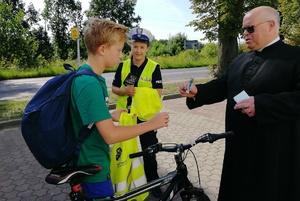 Kapelan wręcza rowerzyście obrazek świętego Krzysztofa, w tle stoi policjantka