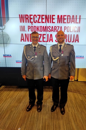 Wyróżnieni medalami policjanci stoją na tle baneru