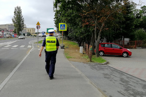 Policjant idzie chodnikiem, sprawdza oznakowanie przy szkole