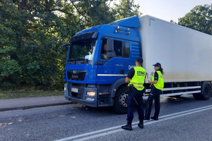 Policjantka wspólnie ze strażnikiem ochrony kolei rozmawiają z kierowcą ciężarówki