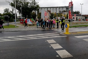 Policjanci wręczają kamizelki grupie dzieci idących chodnikiem