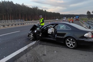 Uszkodzony lewy bok mercedesa, policjant wykonuje oględziny