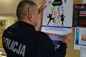 Policjant przywiesza plakat dotyczący mediacji