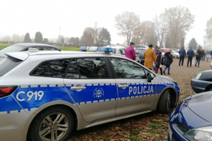 Radiowóz policji na tle idących na cmentarz mieszkańców