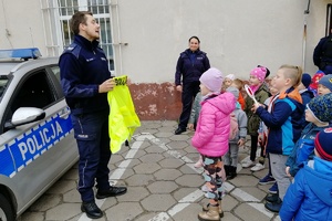 Funkcjonariusz pokazuje dzieciom działanie odblasków na przykładzie kamizelki