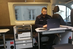 Policjant pracuje przy laptopie wewnątrz radiowozu