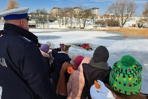 Policjant ruchu drogowego wspólnie z dziećmi obserwuje lekcję straży pożarnej