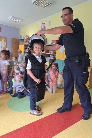 Policjant ubiera chłopcu kamizelkę i hełm ochronny