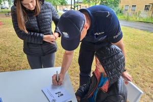 Policjant podpisuje dla dziecka kartkę z odciskami palców