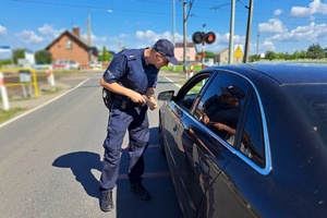 Policjant rozmawia z kierowcą, który zatrzymał się przy przejeździe