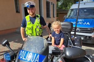 Na motocyklu siedzi dziewczynka, obok stoi policjant