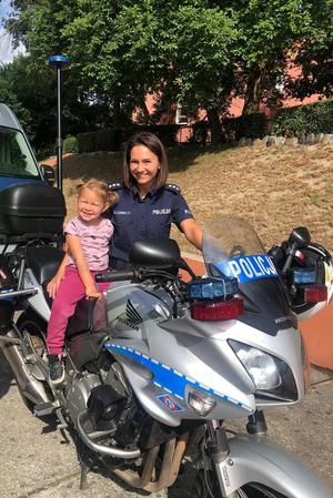 Na motocyklu siedzi dziewczynka, obok stoi policjantka