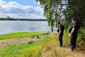 Mundurowi schodzą z górki w rejon plaży przy rzece