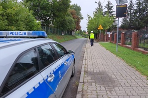 Policjant idzie chodnikiem w rejonie szkoły