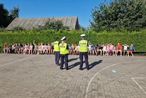 Policjanci stoją przed grupą dzieci, prowadzą spotkanie