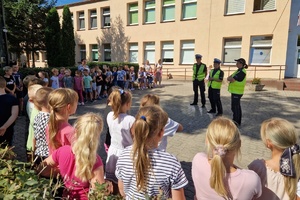 Dzieci stoją na dziedzińcu szkoły i słuchają rad policjantów