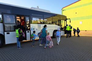 Uczniowie wysiadają z autobusu, policjant prowadzi kontrolę pojazdu