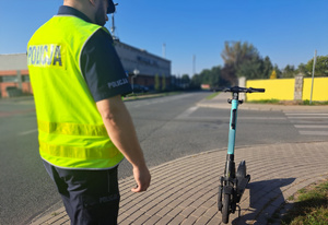 Policjant stoi przy zaparkowanej hulajnodze elektrycznej