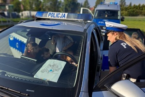 Dzieci siedzą w radiowozie, do nich pochyla się policjantka