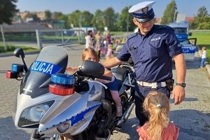 Policjant stoi przy motocyklu i rozmawia z dziećmi