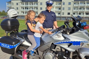 Dziewczynka z chłopcem siedzą na motocyklu policyjnym, obok stoi policjant