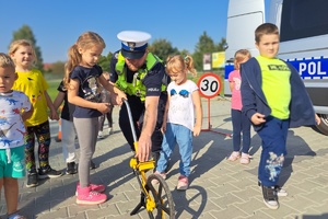 Policjant wspólnie z dziećmi mierzą odległość specjalnym przyrządem