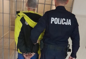 Policjant prowadzi zatrzymanego w kajdankach