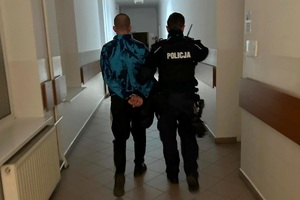 Policjant prowadzi skutego w kajdanki mężczyznę