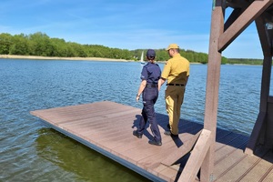 Policjantka wraz ze strażakiem idą pomostem kontrolując zachowania pływających na żaglowce osób
