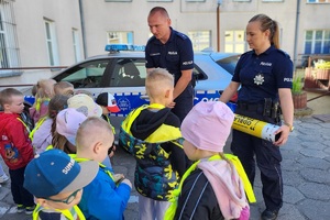 Policjanci stoją na dziedzińcu komendy, rozmawiają z dziećmi