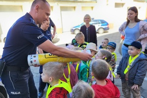 Policjant pokazuje dzieciom na przykładzie tuby działanie odblasków