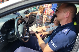 Policjant siedzi w radiowozie, na miejscu pasażera siedzi dziewczynka