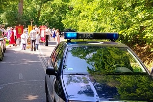 Policjant jadący radiowozem prowadzi uczestników procesji