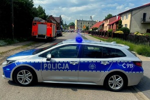 Policyjny radiowóz blokuje ruch pojazdów podczas przemarszu procesji
