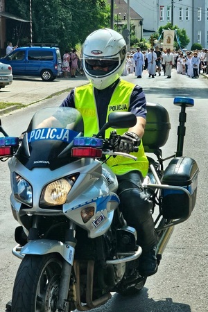 Policjant jadąc motocyklem prowadzi przemarsz procesji